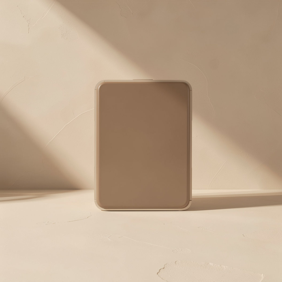 Foldmate Foldable Metal Phone Stand – folded flat tan stand standing upright against a textured beige wall in soft sunlight