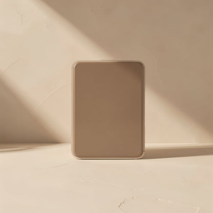 Foldmate Foldable Metal Phone Stand – folded flat tan stand standing upright against a textured beige wall in soft sunlight