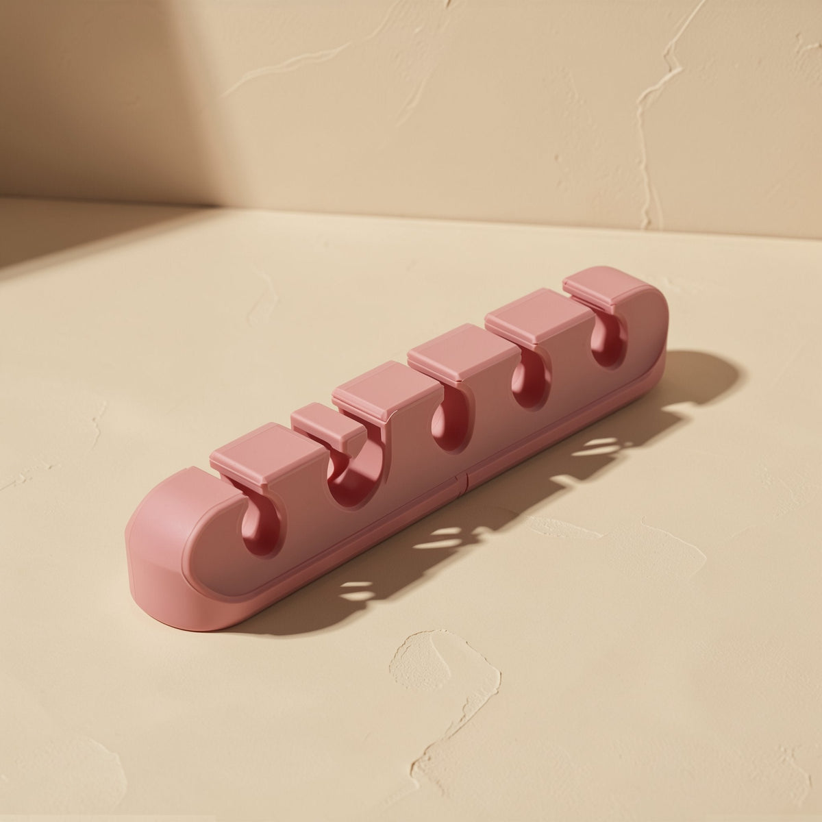 Cordcoil Silicone Data Cable Organizer in dusty pink, angled view of five cable slots on a beige surface