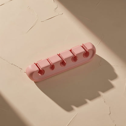 Cordcoil – Top-down view of pink five-slot cable holder with round openings, casting long shadows on a plaster surface