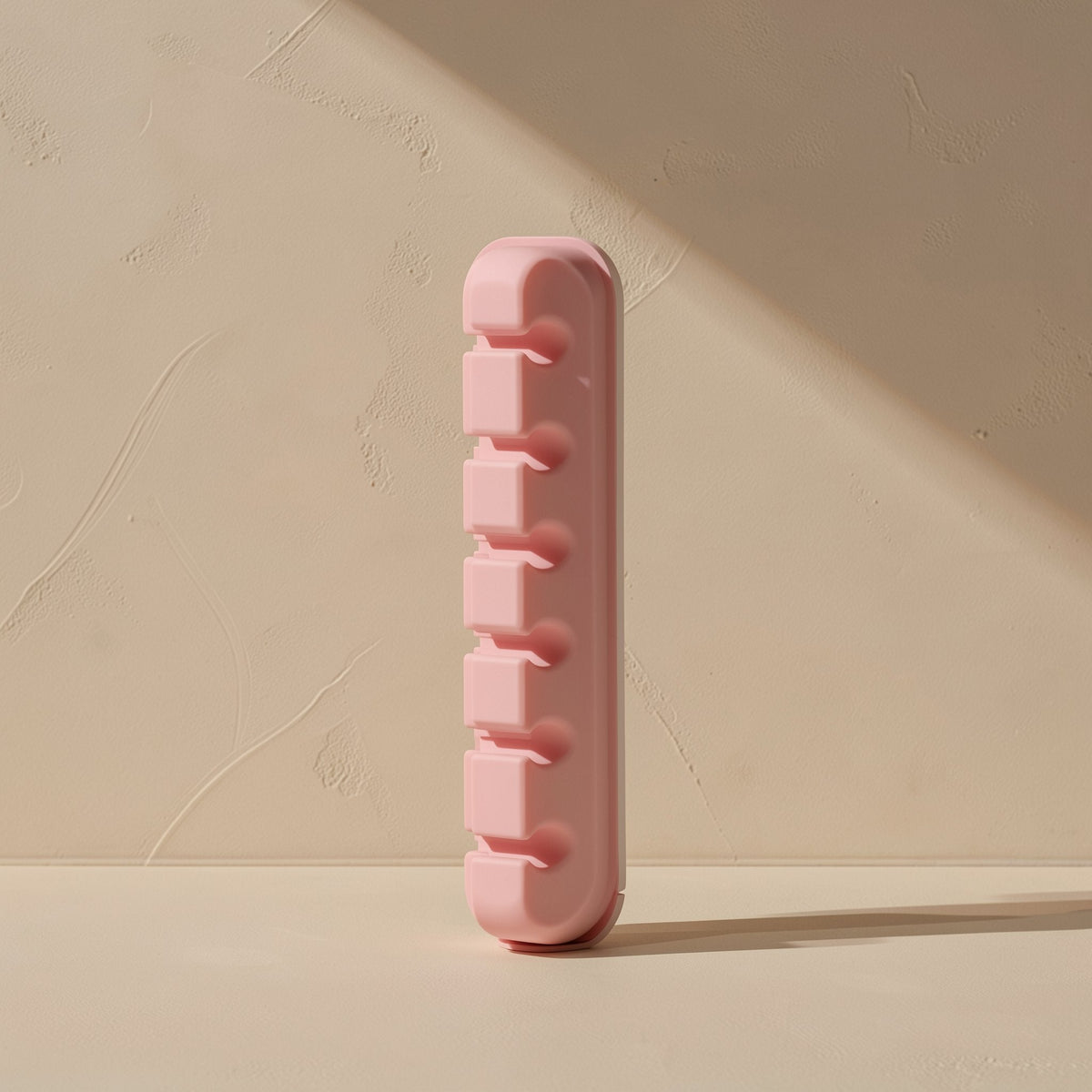 Cordcoil – Pink silicone cable clip standing upright, showing five slots stacked along its side against a textured wall
