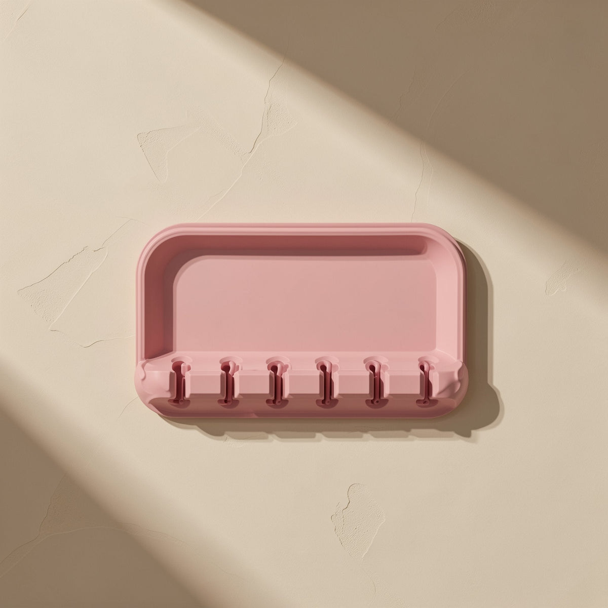Cordcoil – Pink silicone tray with six narrow cable slots along the front edge, seen from above on a beige background