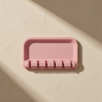 Cordcoil – Pink silicone tray with six narrow cable slots along the front edge, seen from above on a beige background
