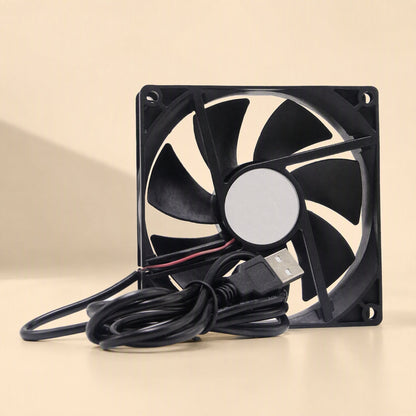 Coolbyte – Fan seen head-on with a plain grey sticker on the center hub, USB cable looped below on a beige surface