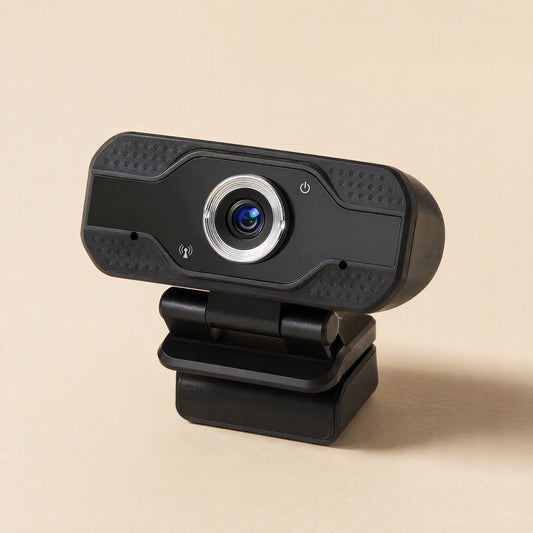 Camclear USB Webcam – black webcam seen from the front left, tilted on its folded clip base against a plain tan backdrop