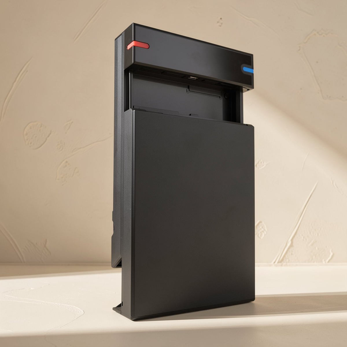 Drivestow – Black enclosure with red and blue tabs and its front cover slid open, standing on a beige surface