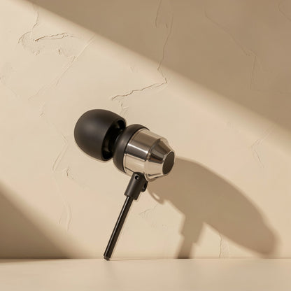 Cordtone wired in-ear headphone with black ear tip and silver metal housing leaning against a beige wall