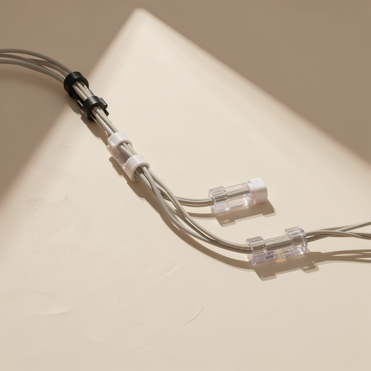 Stickloop – Gray cables held along a beige surface by clear, white and black self-adhesive cable clips