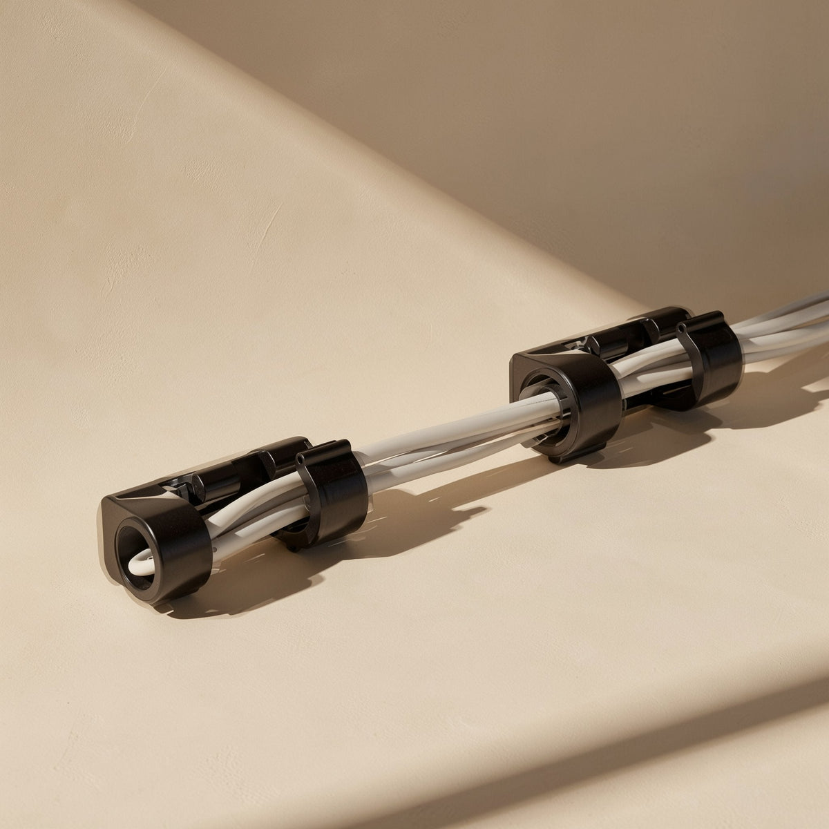 Stickloop – Pair of black cable clips holding a bundle of white cables on a beige surface, shown at a low angle