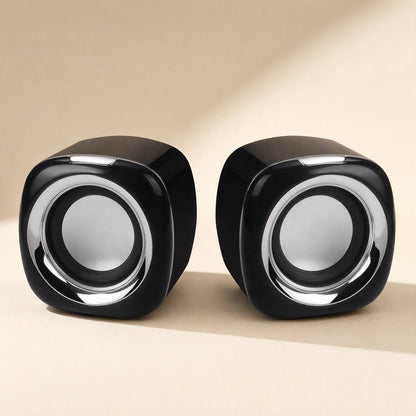 Deskvoice – Pair of black cube-shaped desktop speakers with silver rings around the round grey drivers, front view