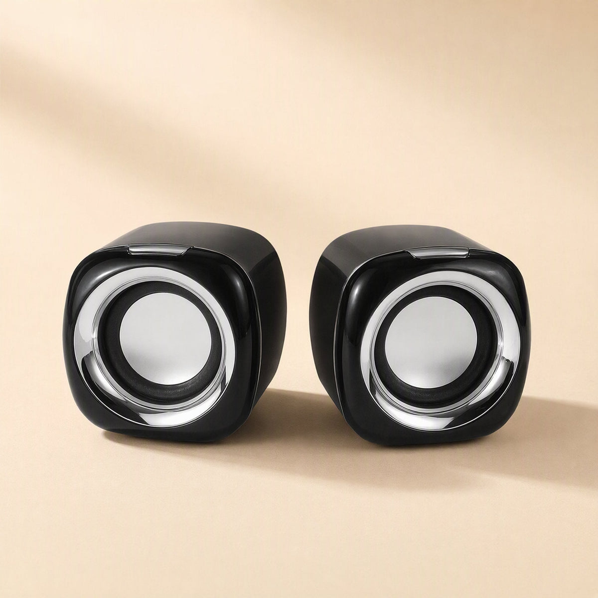 Deskvoice – Two glossy black square speakers with silver ring detail on a warm beige surface, seen head-on