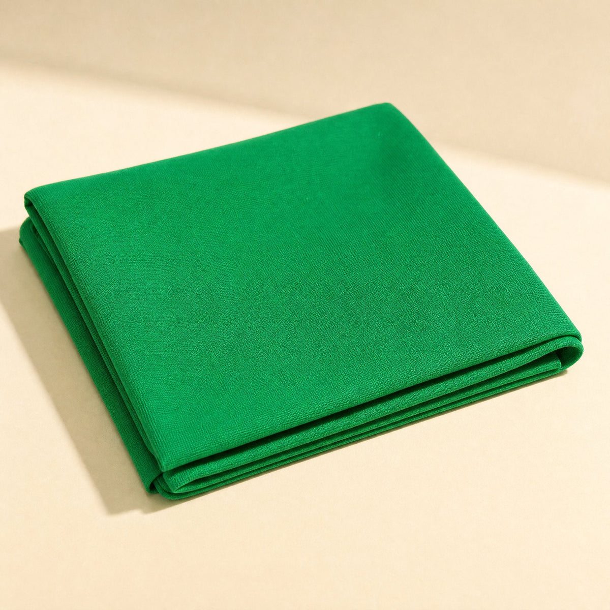 Screenweave – Green background cloth folded into a neat square on a cream surface, showing the fabric texture