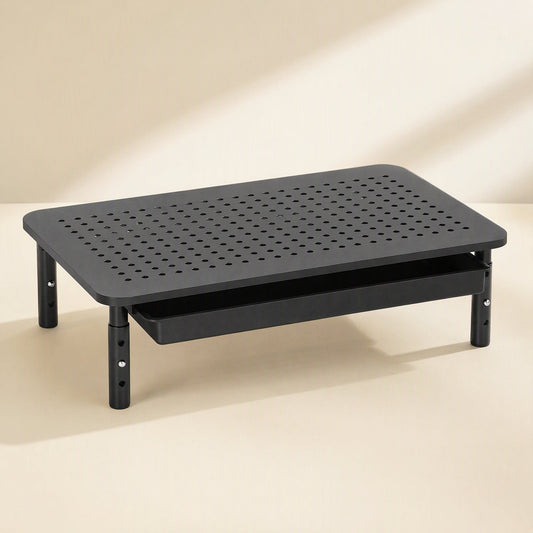 Alloydesk – Black perforated desktop stand with slim drawer closed underneath and height-adjustable legs on a cream backdrop