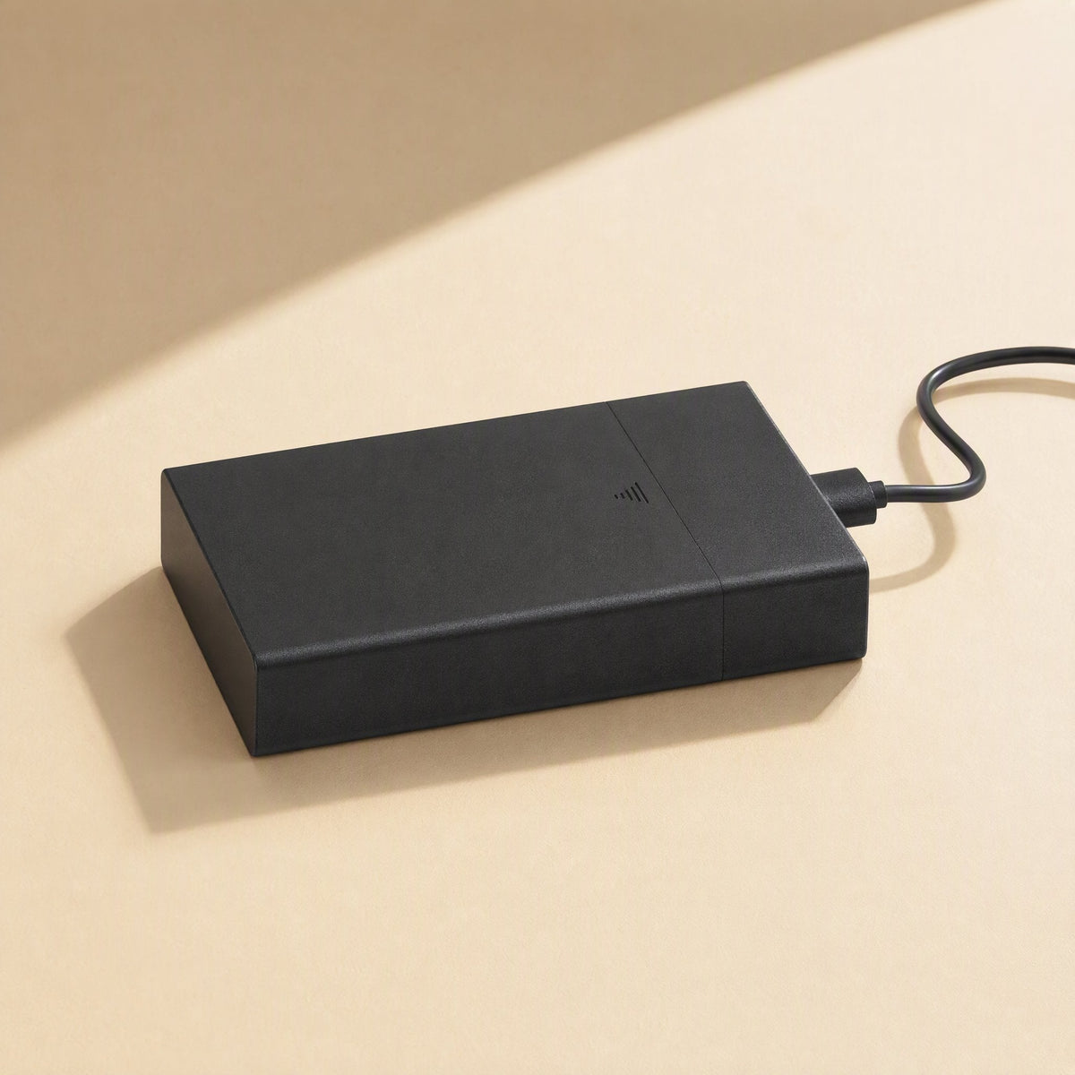 Satavault – Black enclosure lying flat with a USB cable plugged into its end, in soft window light