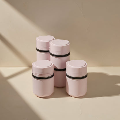 Tiltfold – Four pink cylindrical lidded containers with black bands stacked in two tiers on a cream surface