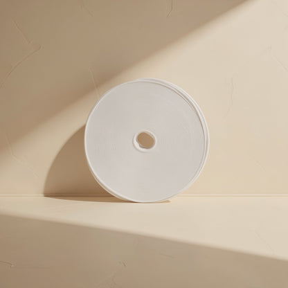 Wrapcord – White roll of hook-and-loop tape standing on edge against a cream wall, seen from the front