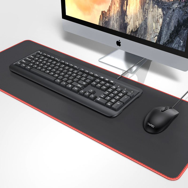 Rubberglide – Large black desk mat with red edge under a keyboard and mouse in front of an iMac