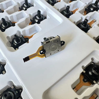 Driftfree – Back of the joystick module showing its metal casing and orange flex cable, with more units in the tray
