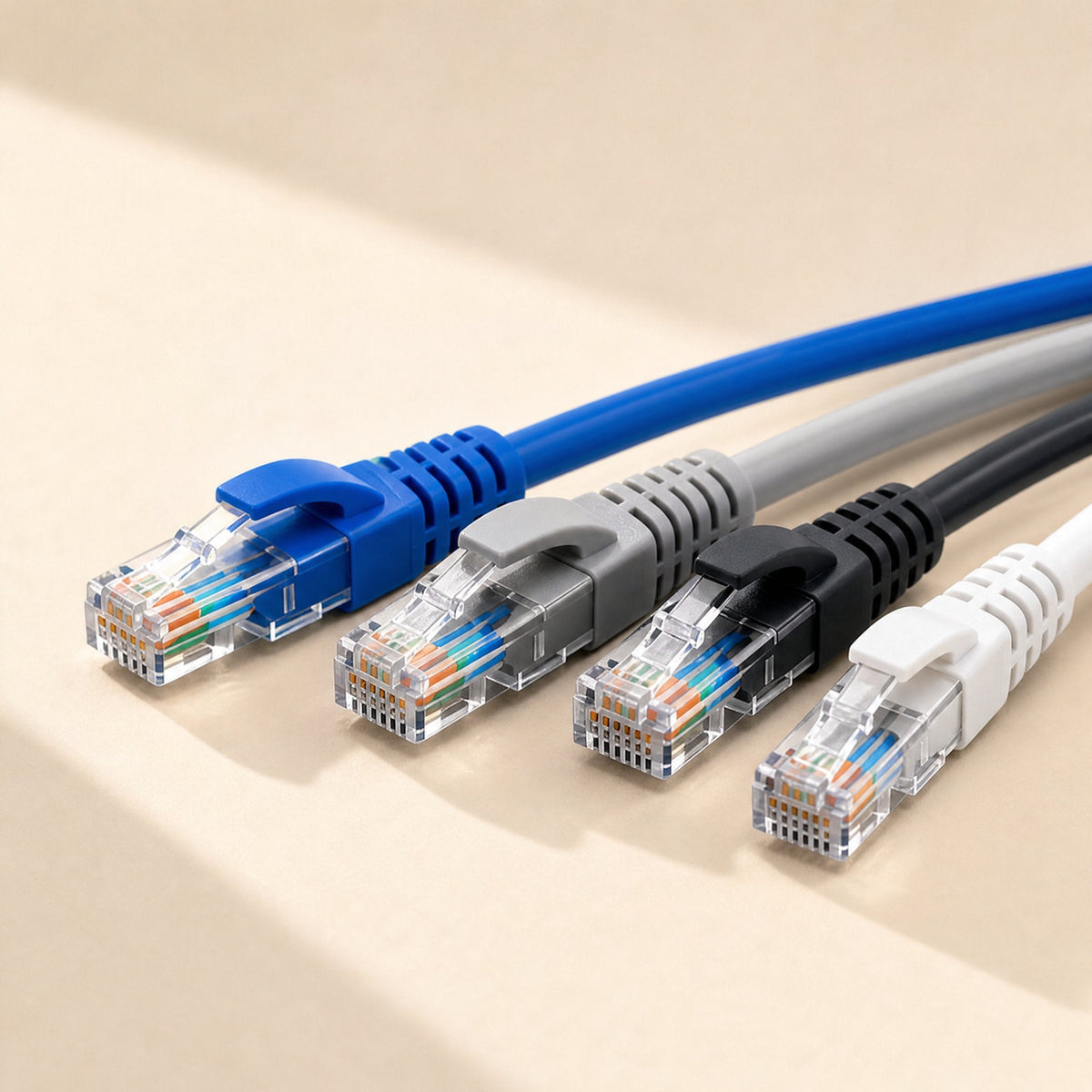 Copperlink – Four patch cables in blue, grey, black and white with clear RJ-45 plugs lined up on a cream surface
