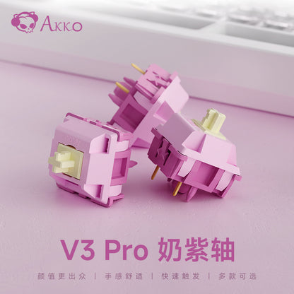 Keygrove – Three pink switches with pale yellow stems on a lilac surface, labeled V3 Pro, with a keyboard behind