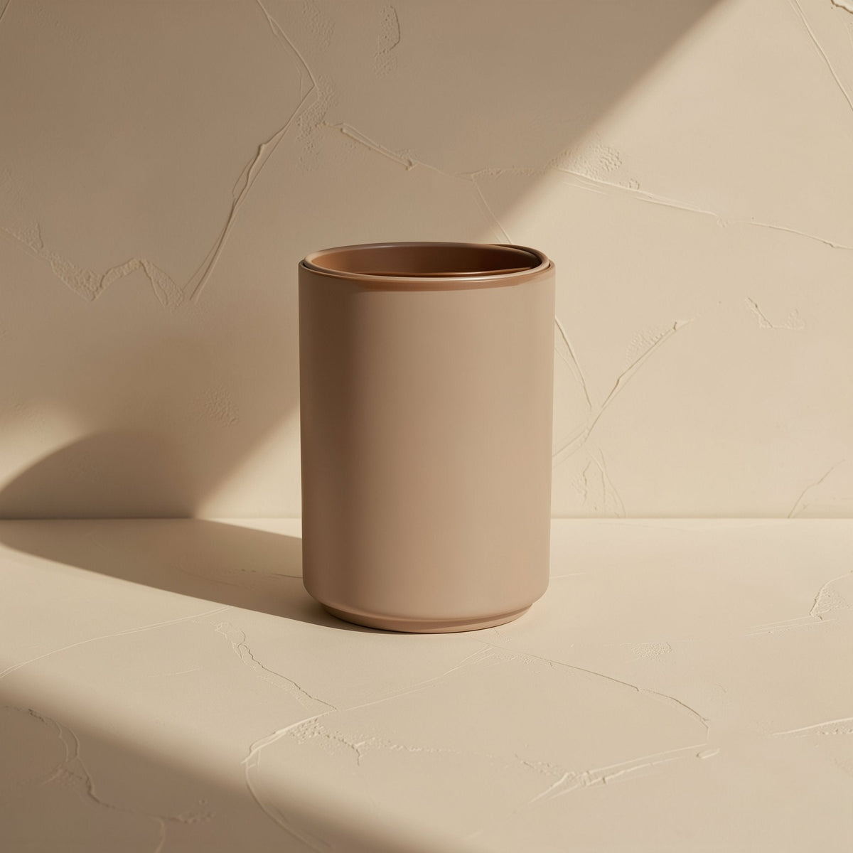 Aluperch – Matte taupe cylindrical cup with a brown rim on a plaster-textured beige surface in angled sunlight