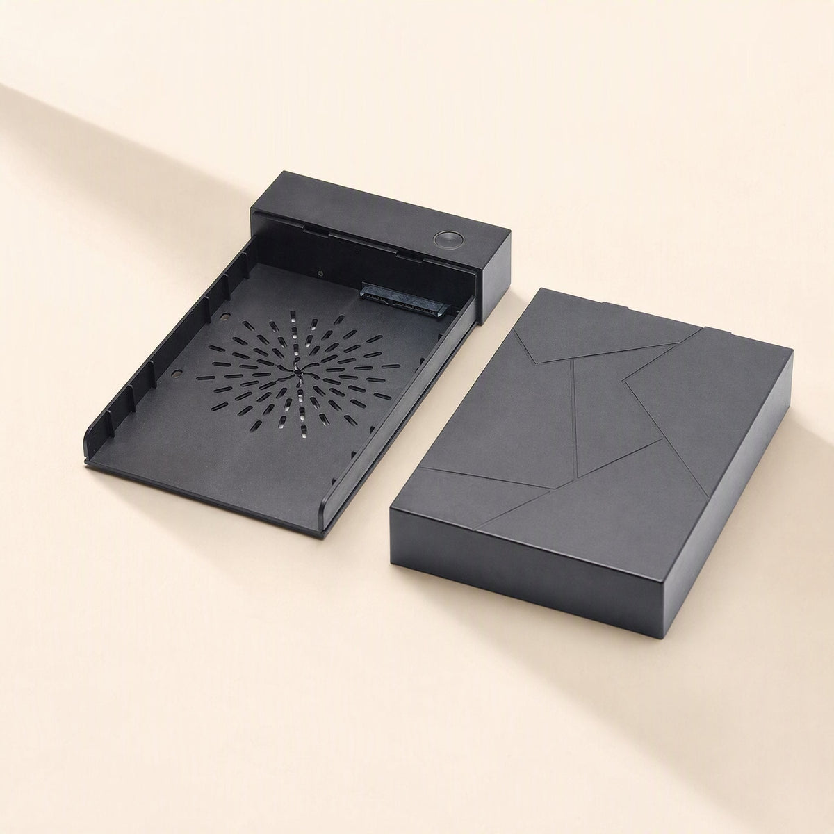 Diskbox – Empty black enclosure tray with SATA connector and vent pattern, next to its separated geometric-patterned lid