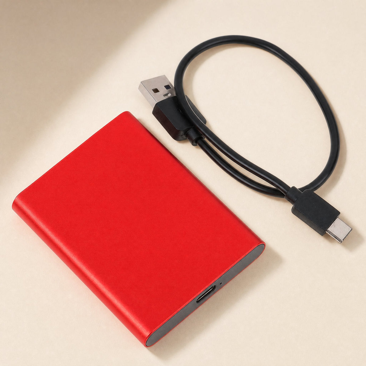 Shellswift Mobile Solid-State Drive – red portable drive lying flat beside a black USB-A to USB-C cable coiled next to it