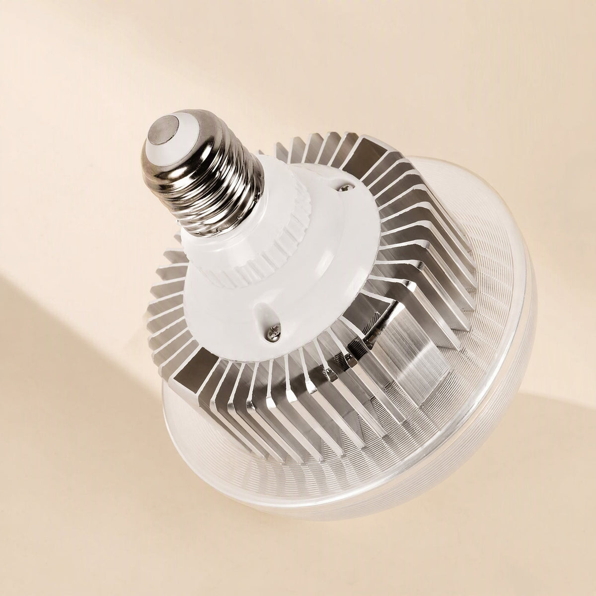 Faceglow – Close-up of an E27 LED bulb with silver heat-sink fins, white base and clear ribbed lens on a beige background