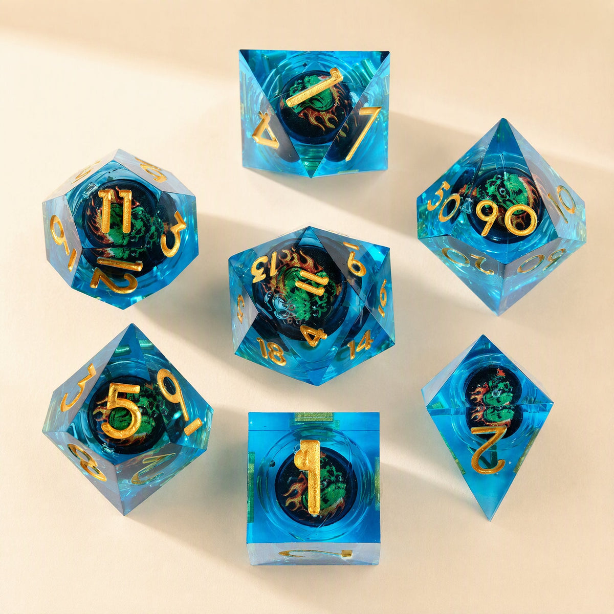 Fateforge – Blue resin dice set with gold numerals and a green dragon surrounded by flames, seven dice arranged on cream