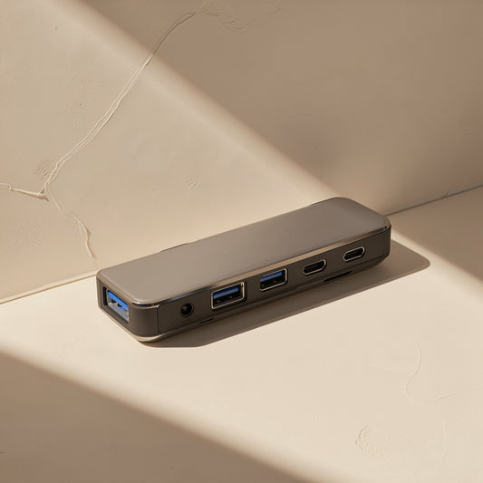 Aludock – Silver-grey hub with USB-A and USB-C ports and audio jack, resting on a sunlit beige ledge
