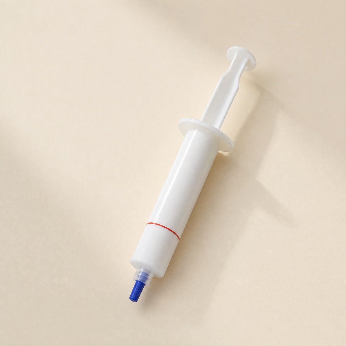 Silkspread CPU Thermal Paste – single white syringe with a thin red band and blue tip, shown at an angle on a cream surface