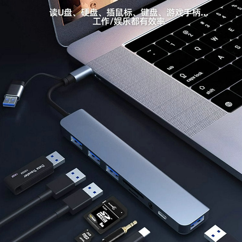 Voltcast – Hub plugged into a laptop's side with a USB drive, cables, SD card and audio plug laid out nearby