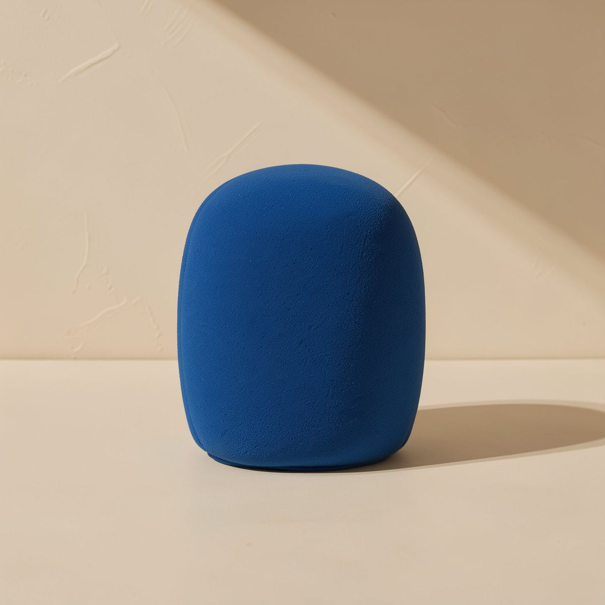 Micmuffle – Single blue foam microphone cover standing upright against a textured beige wall in angled sunlight