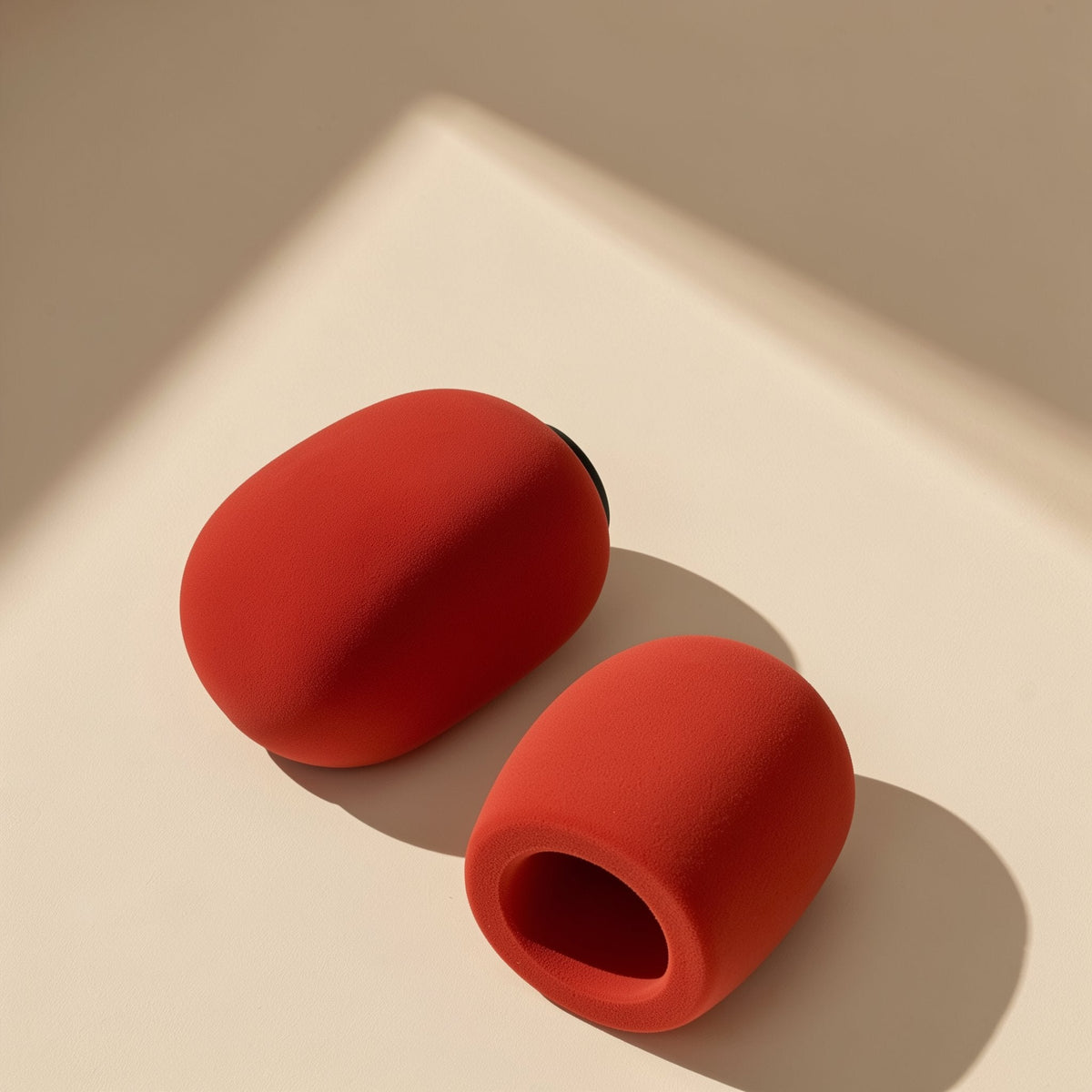 Micmuffle – Two red foam microphone covers on a cream surface, one lying on its side and one showing its open end