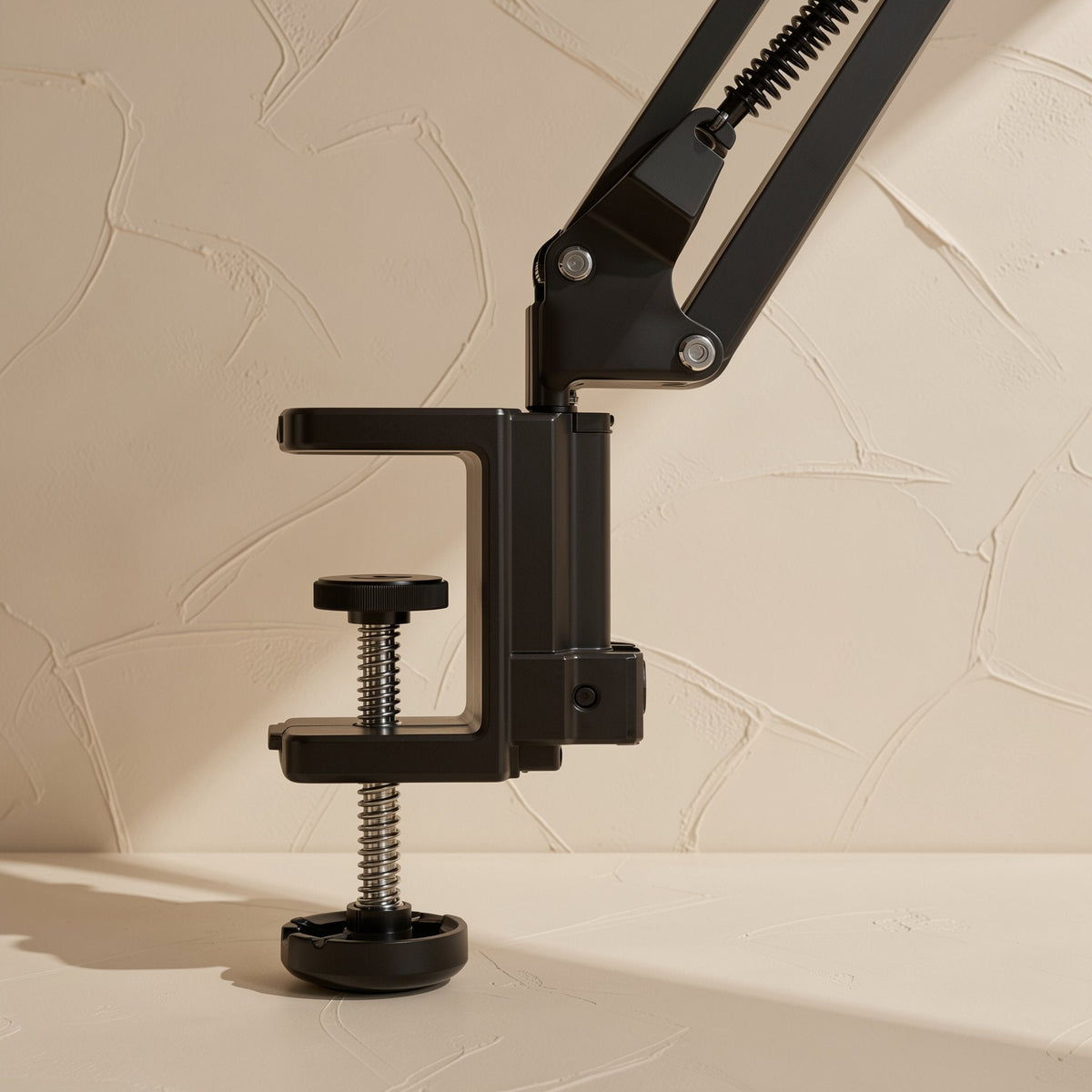 Clampmate – Close-up of the black C-clamp base with threaded screw knob and rubber foot at the arm's lower joint