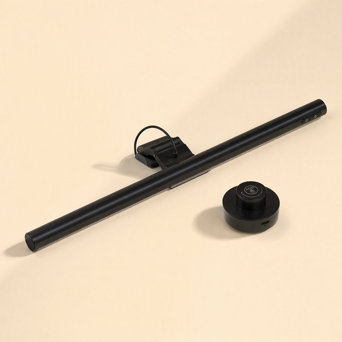 Glowhang – Black light bar lying beside a round black wireless control puck on a beige background
