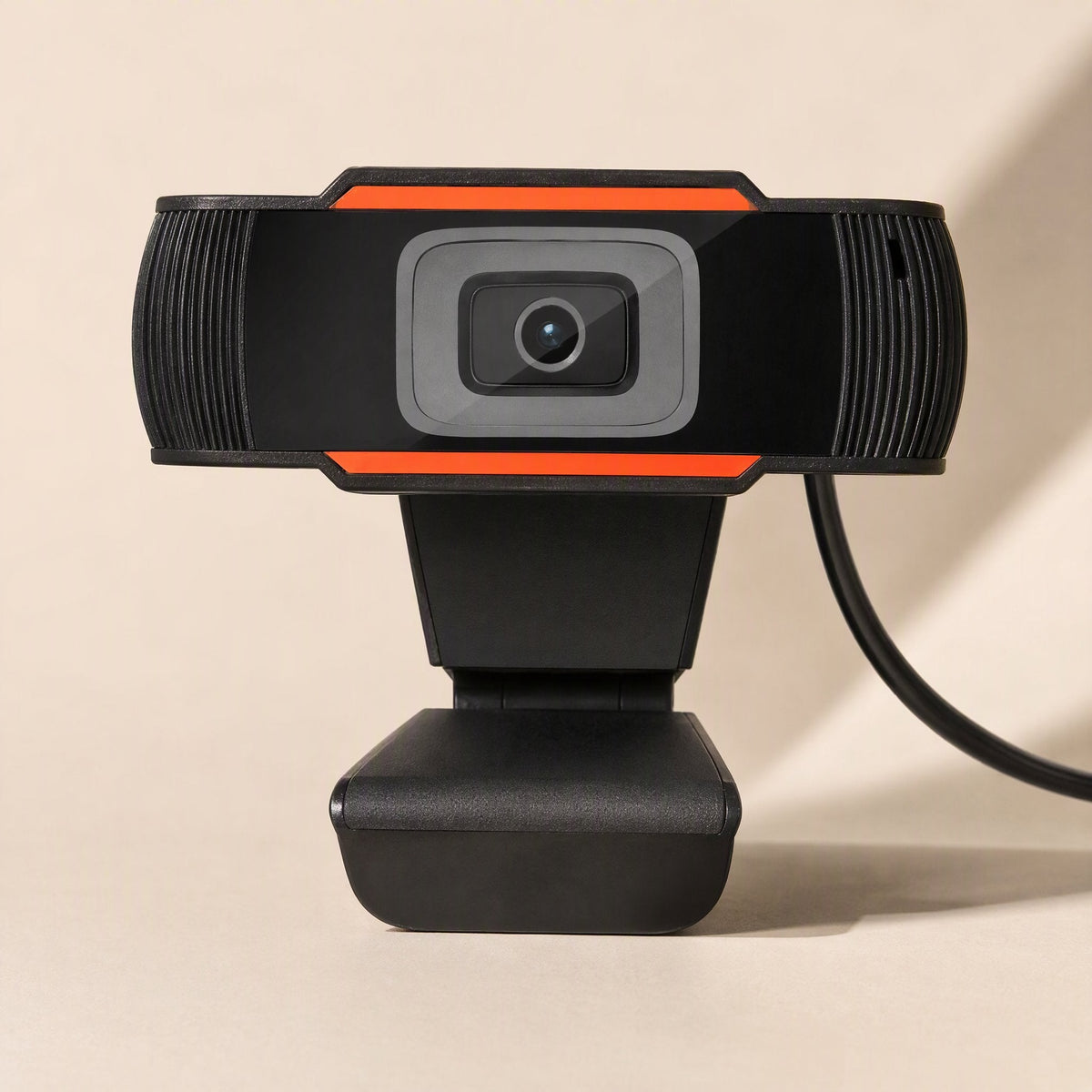Voicelens – Front view of the black webcam with orange stripes, ribbed side grilles and USB cable trailing to the right