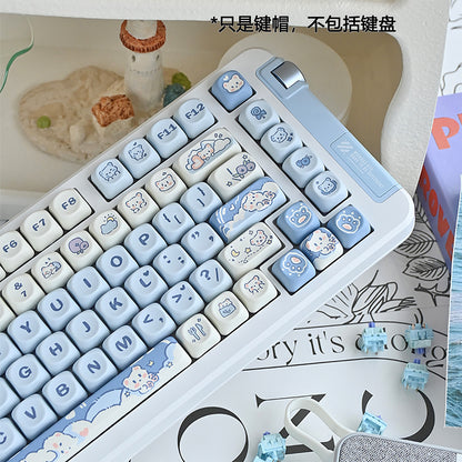Cubicle Ice Cream Bear keycaps in blue and cream on a white keyboard, angled view beside a small lighthouse