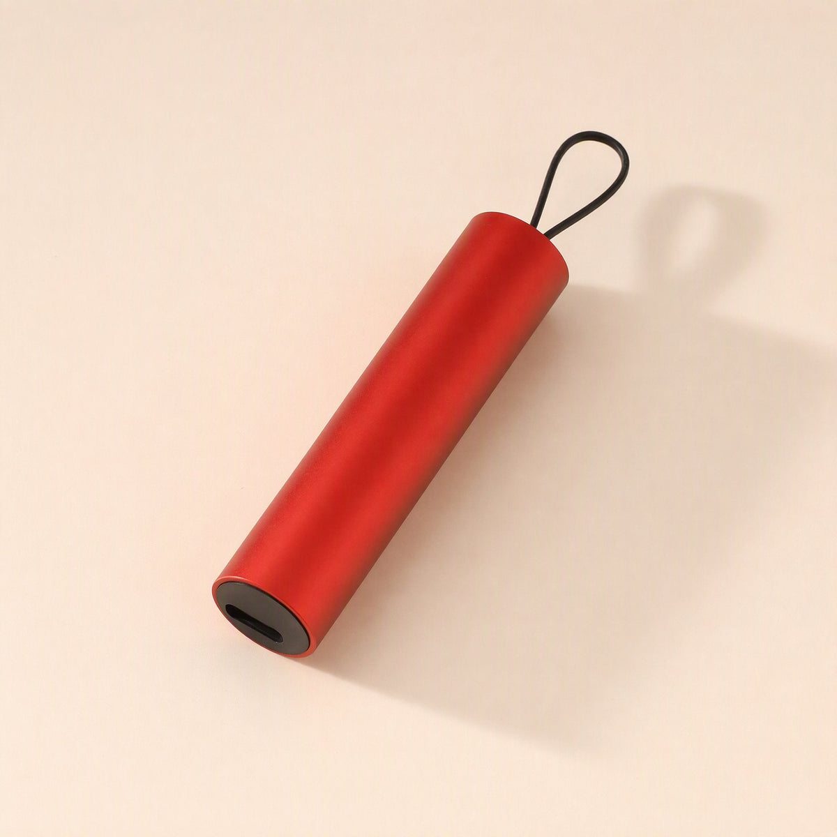 Quickcord – Red cylindrical cable case with a black loop and a port at one end, lying on a peach backdrop