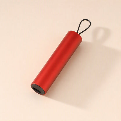 Quickcord – Red cylindrical cable case with a black loop and a port at one end, lying on a peach backdrop