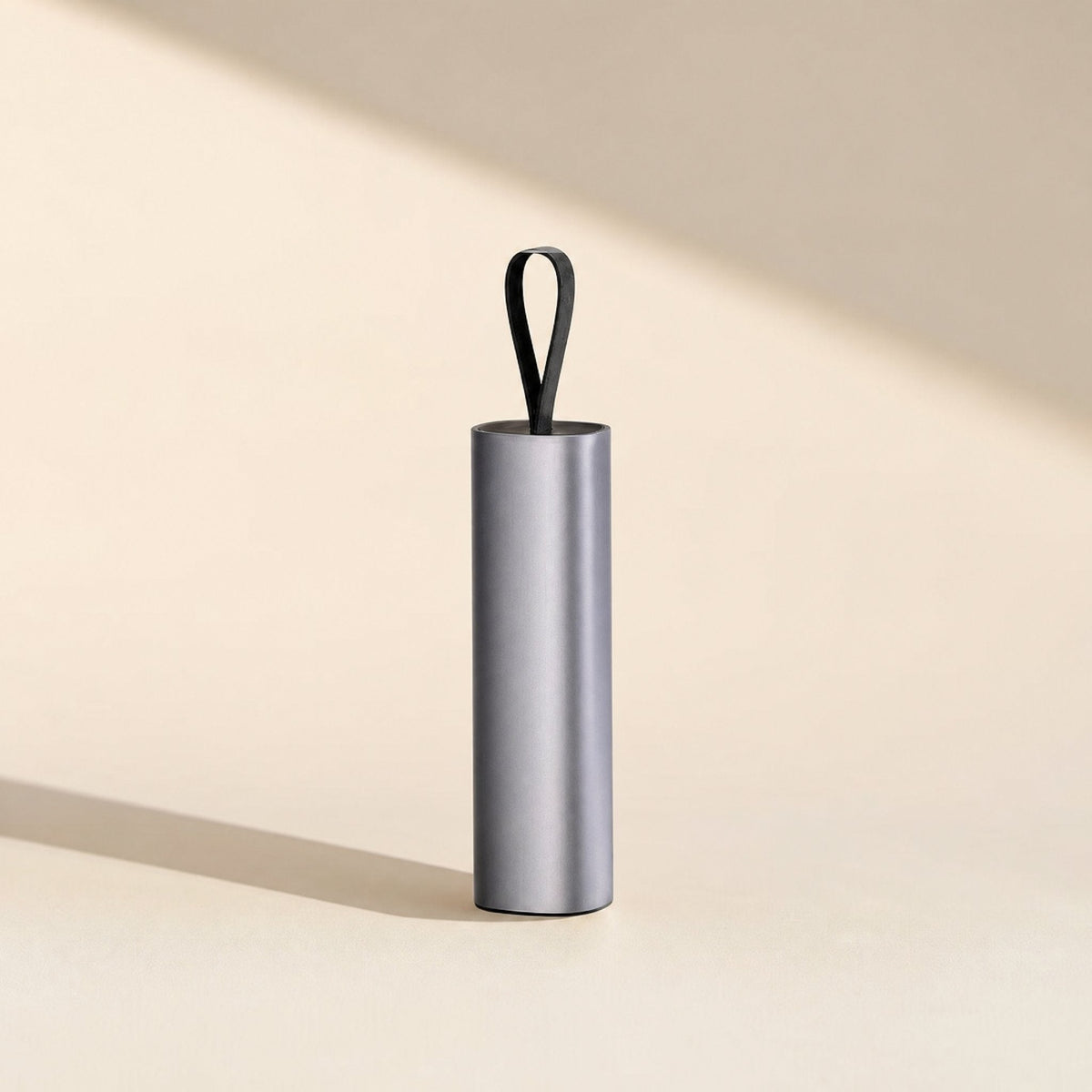 Quickcord – Grey aluminum cable cylinder standing upright with a black loop on top, casting a long shadow