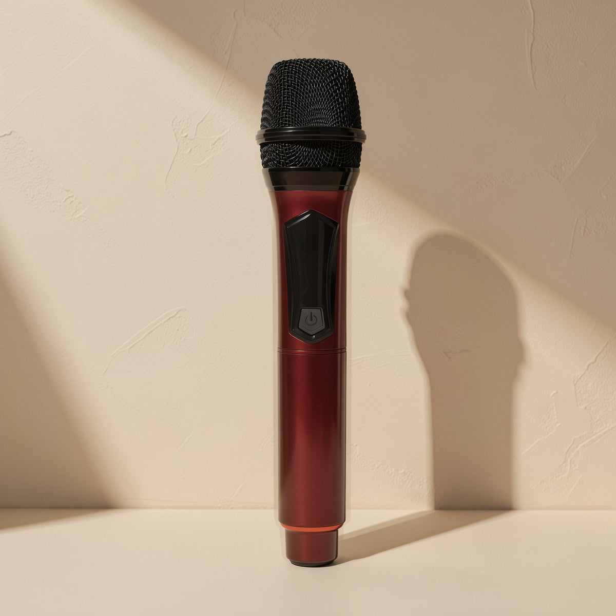 Voicevolt – Handheld microphone in deep red with a black mesh head and orange base ring, standing in soft shadow
