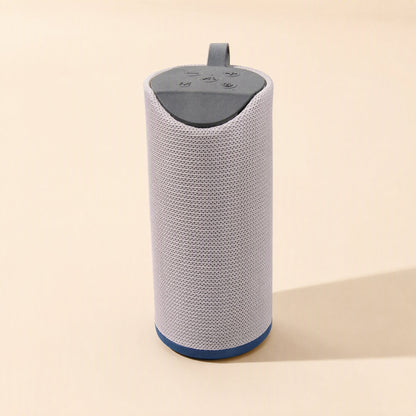 Tuneclip – Light grey fabric speaker with dark grey top panel, small strap and blue base, standing upright