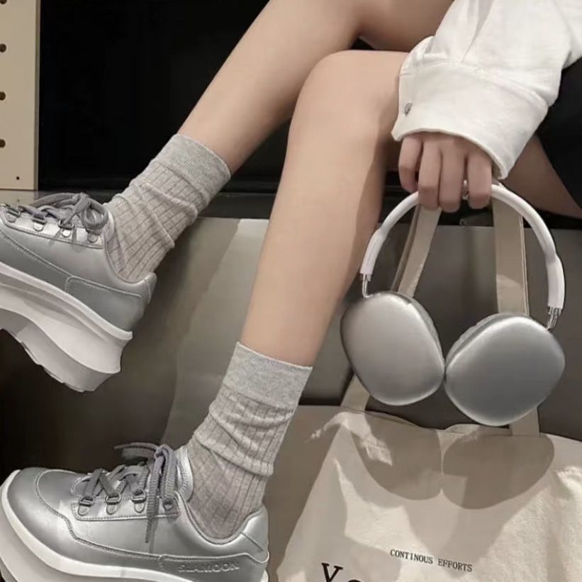 Basswave – Silver over-ear headphones held by the headband beside crossed legs in grey socks and silver sneakers