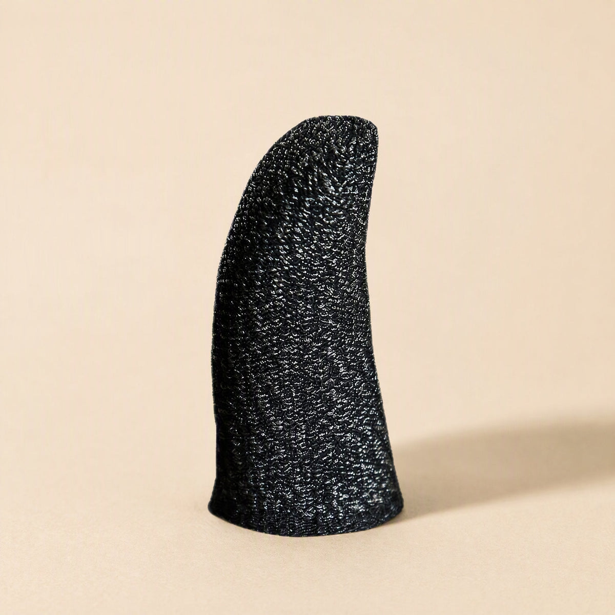 Gamegrip – Single black finger sleeve with silver fiber knit texture standing upright on a beige background