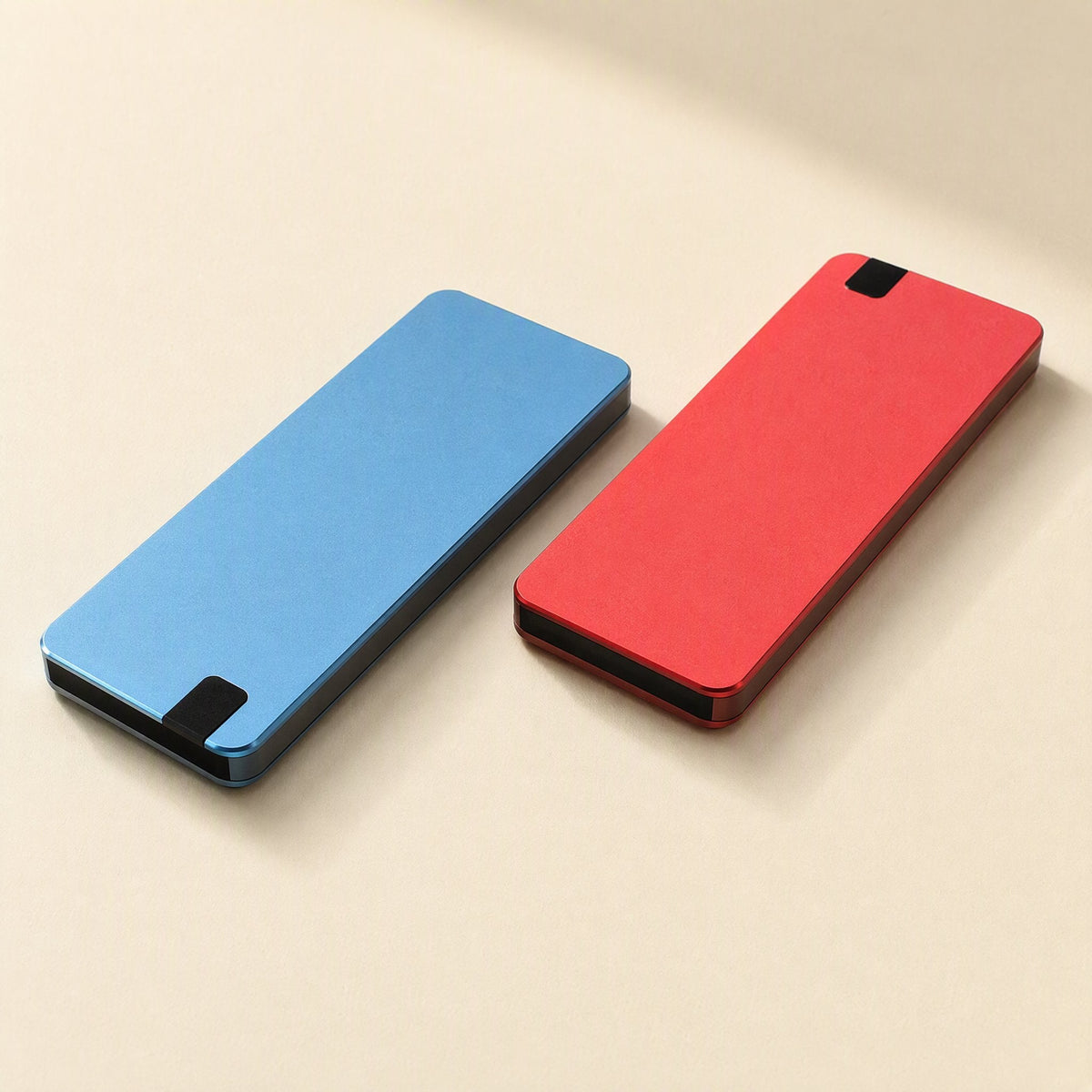 Solidvault Portable SSD – blue and red slim metal drives lying side by side on a cream surface, each with a black end tip