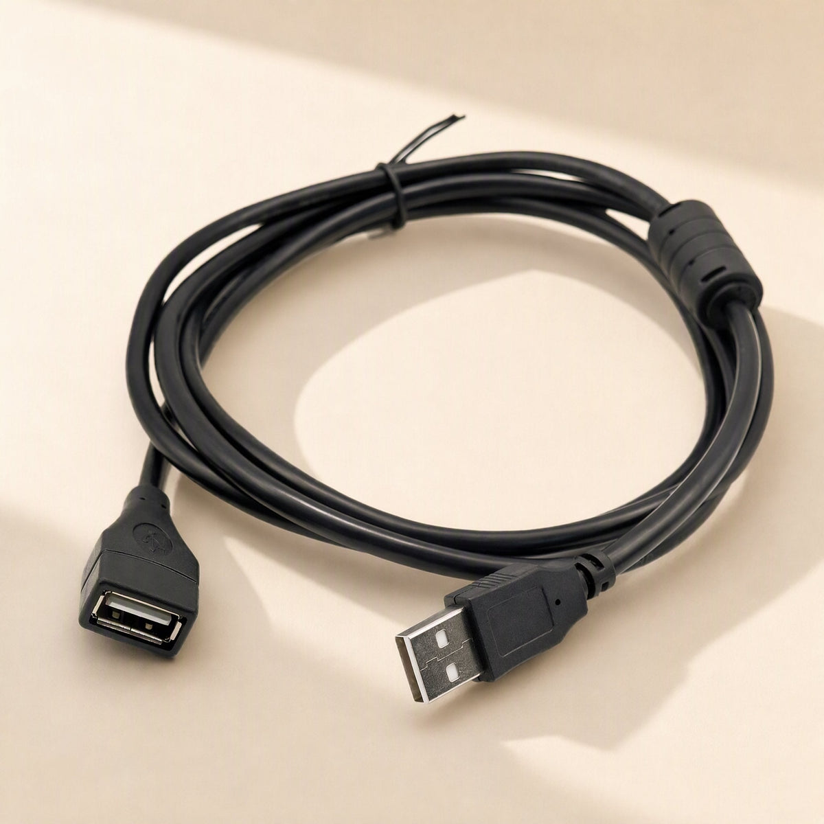 Copperreach – Black extension cable looped in a wide coil with the USB A plug and socket both visible, beige surface