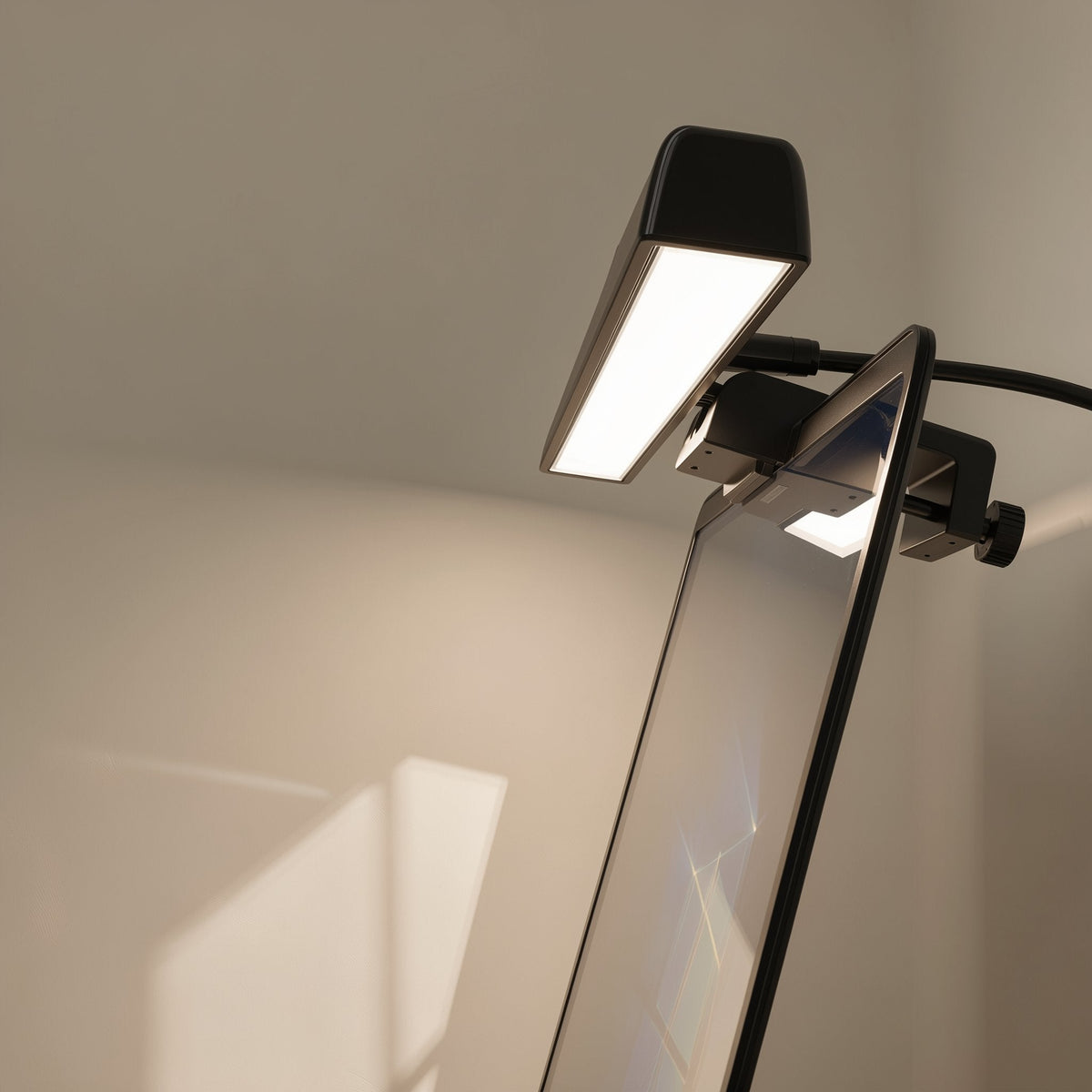 Taplume – Close-up of a black screen lamp with glowing light panel clipped to a monitor edge with a thumbscrew