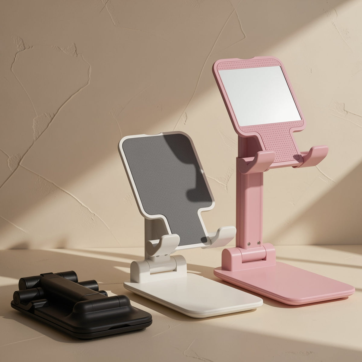 Foldstand – White, pink and black folding phone stands on a beige surface, the black one folded flat
