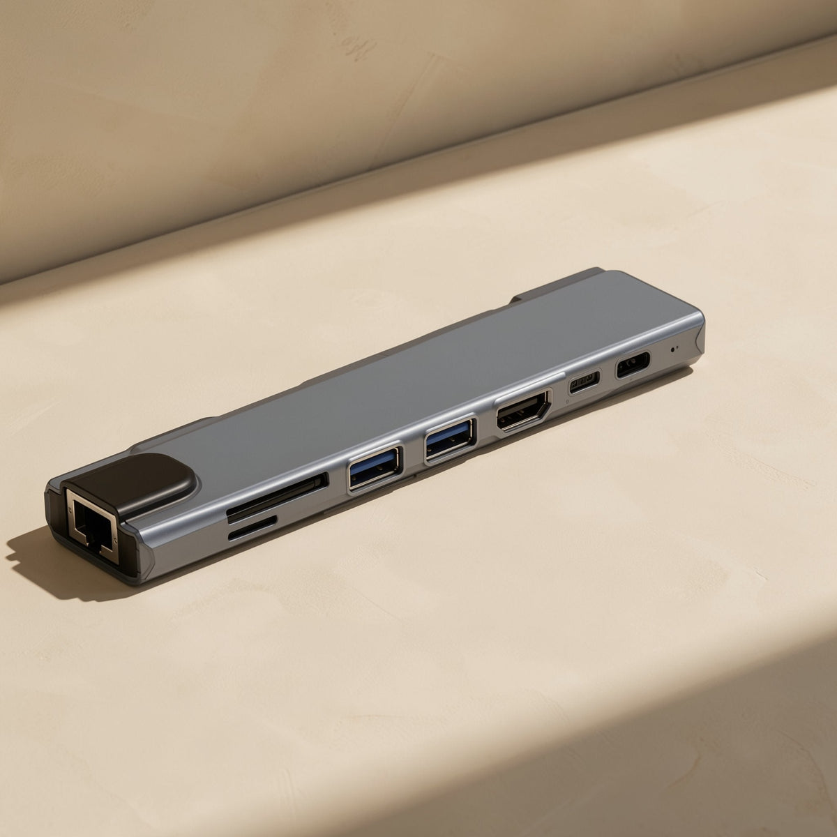 Docknest USB-C docking station hub in grey lying flat on a beige surface, ports facing the camera